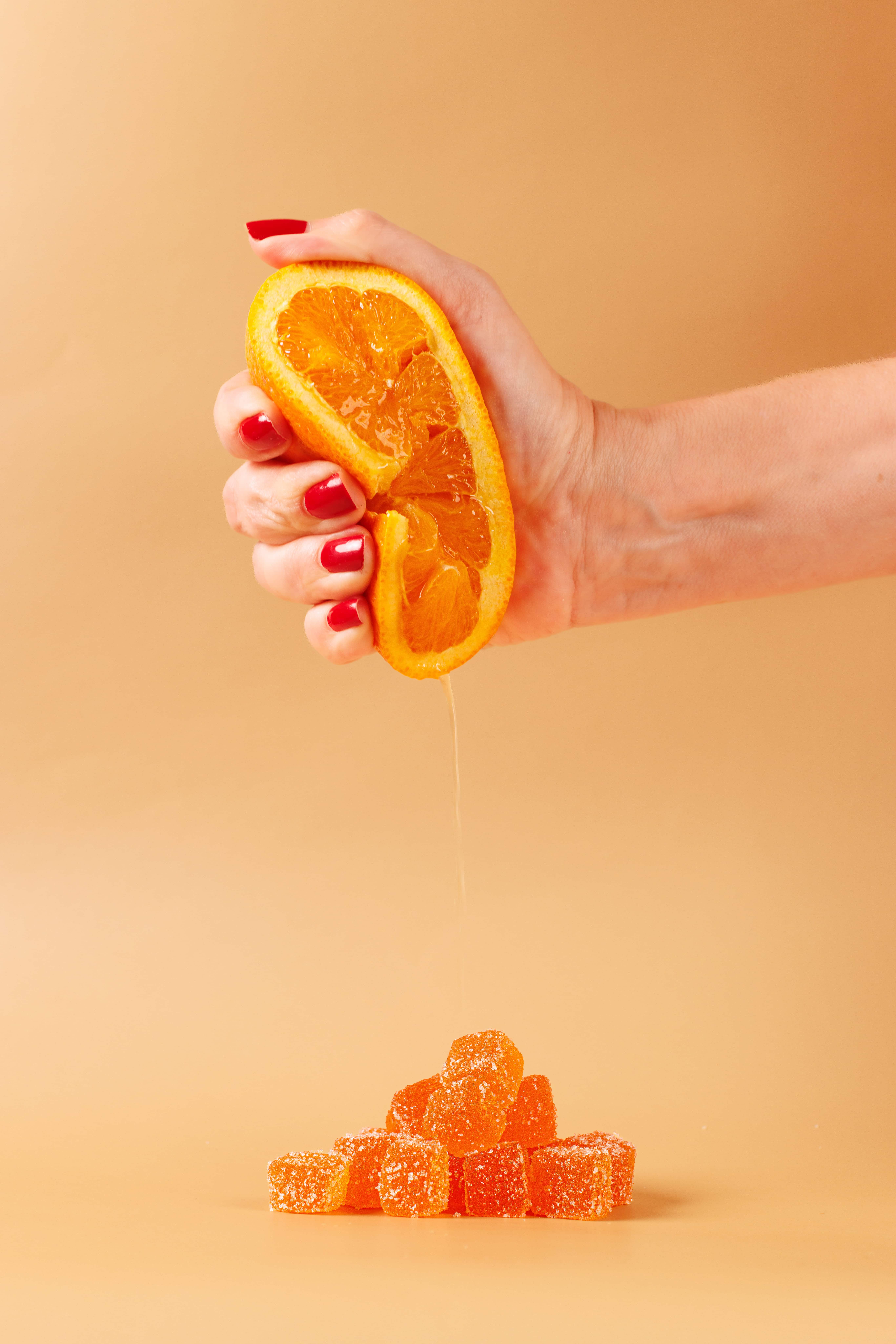 Juice squeezed from fresh orange slices dripping onto sugar-coated orange gummy candies, representing natural ingredients and flavor in confectionery and formulation products.