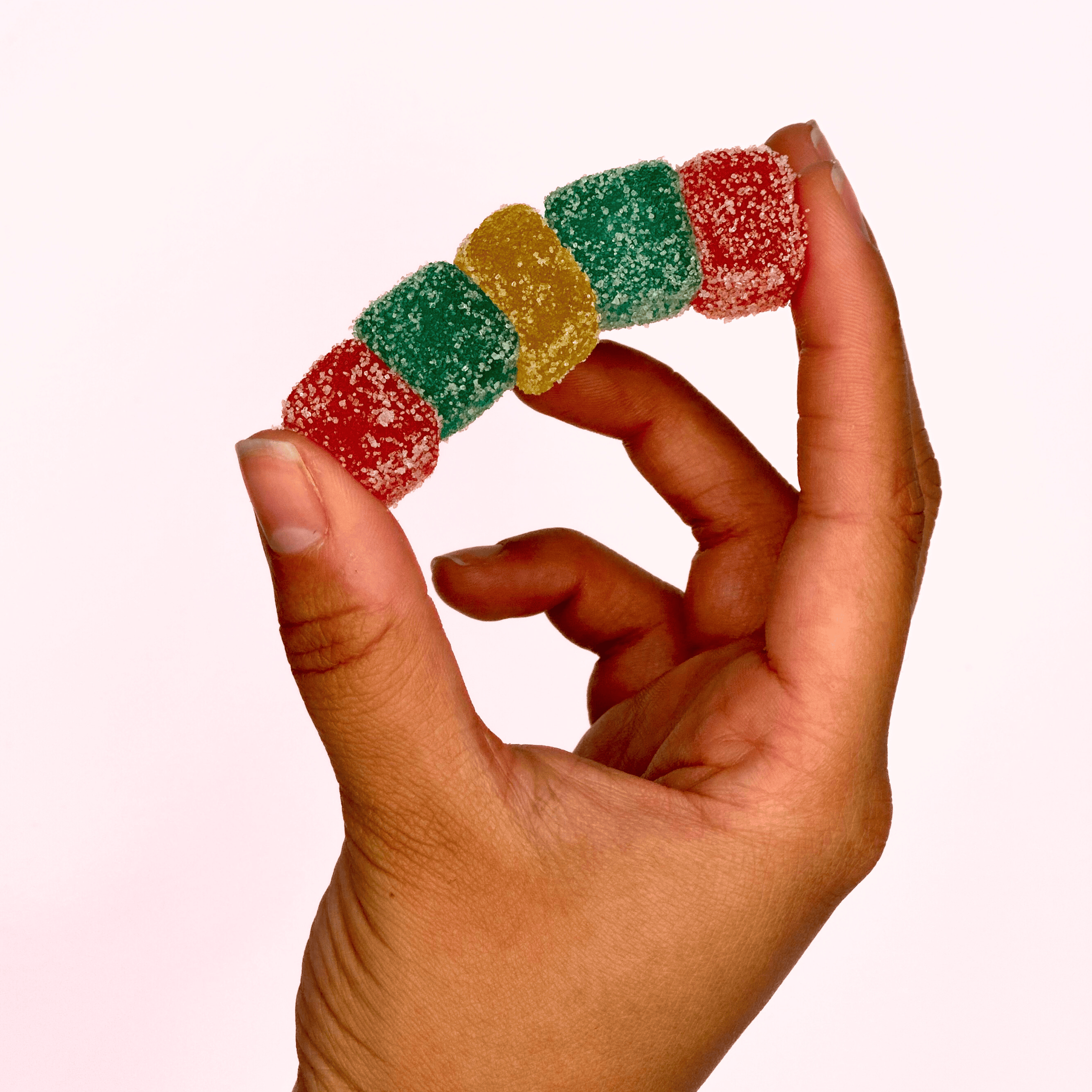 Colorful fruit-flavored gummy candies covered in sugar, held between fingers showcasing snacking options and sweet treats.